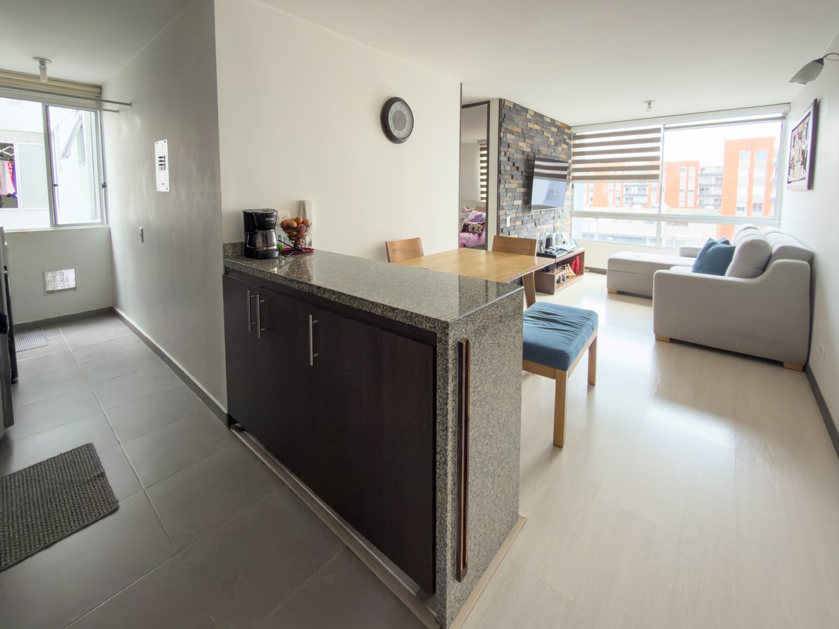 Cocina con barra y sala del apartamento, con ventanal al fondo.